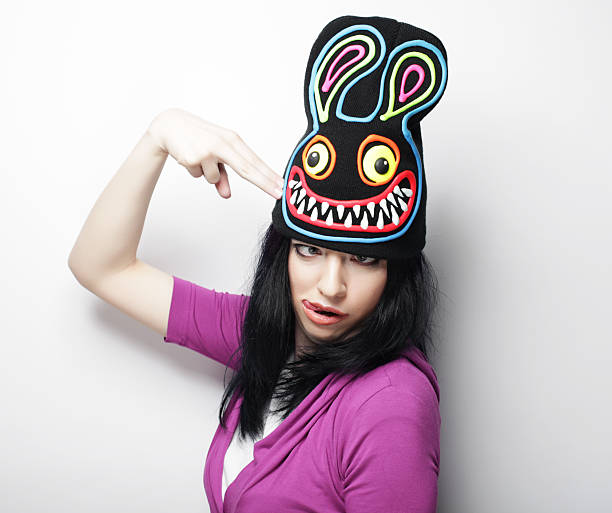Playful young woman in funny hat with rabbit, studio shot