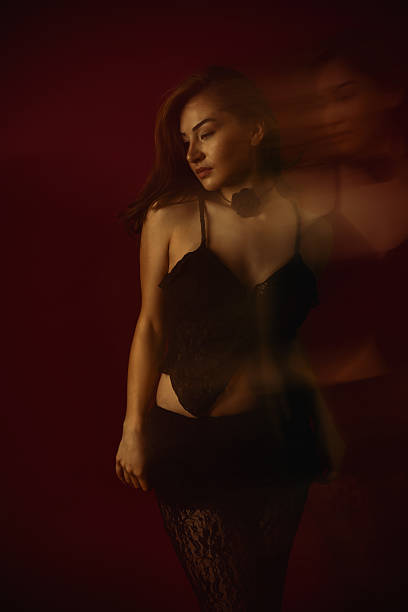istock Beautiful Female Posing on Dark Red Background While Wearing Black Lace Outfit 2214063235