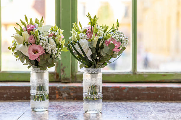 Two beautiful wedding bouquets with pink and white flowers resting on a windowsill in decorated glass jars