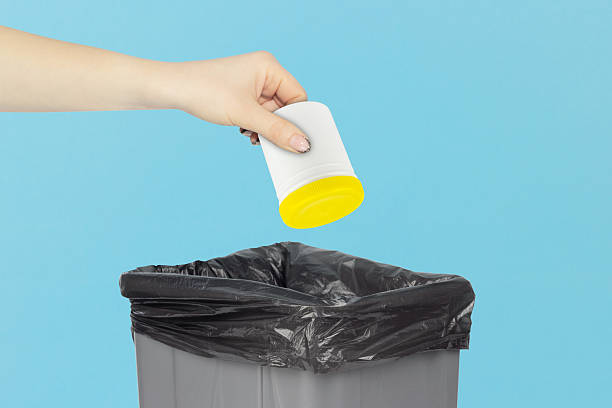 istock throwing plastic jar with vitamins into trash, outstretched hand with plastic jar with vitamins in front of trash can 2214070193