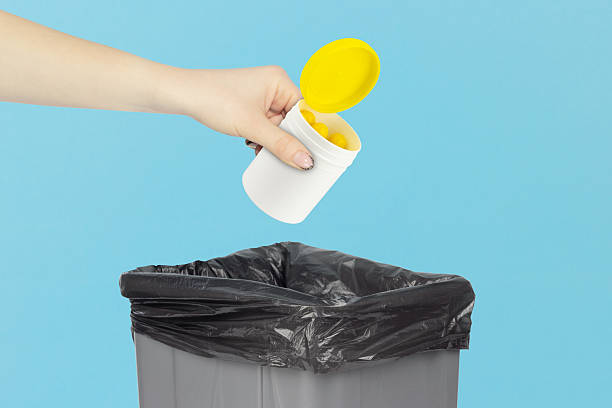 istock throwing plastic jar with vitamins into trash, outstretched hand with plastic jar with vitamins in front of trash can 2214070196