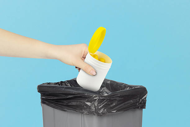 istock throwing plastic jar with vitamins into trash, outstretched hand with plastic jar with vitamins in front of trash can 2214070198