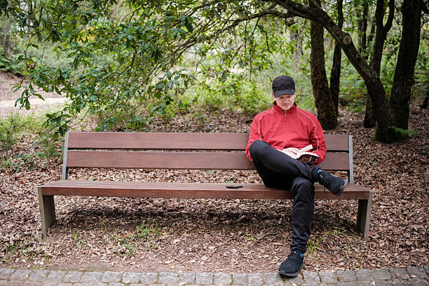 adult man is sitting on a park bench, engrossed in reading a book, enjoying the tranquility of nature