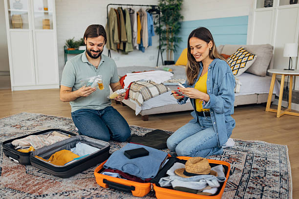 istock Carefree man putting plastic cosmetic airplane kit into suitcase while packing for a trip with his girlfriend 2214073666