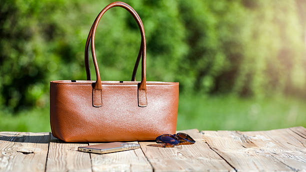 istock Spring composition on wooden table with smartphone, sunglasses and handbag set against blurred garden. Mother's day or Women's day or greeting card background with copy space. 2214074161