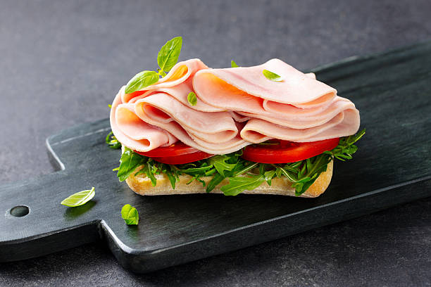 istock Ham sandwich with fresh tomatoes, green salad and cheese on a black marble board. Dark grey background. Close up. 2214075320