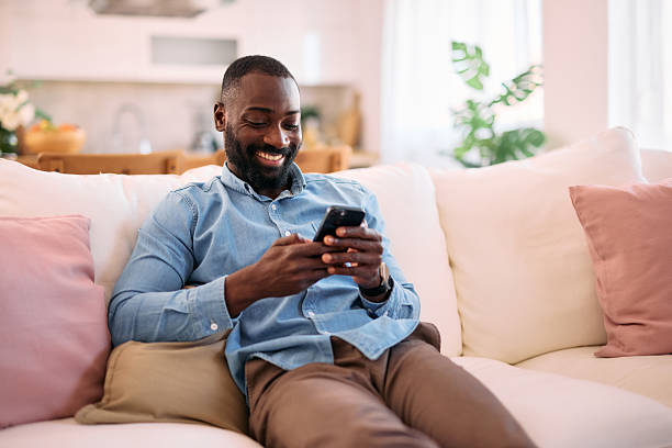istock Smiling man relaxing on sofa using mobile phone at home 2214076780