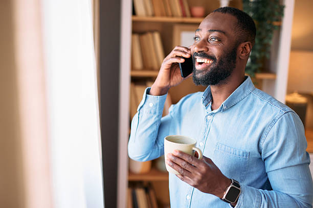 istock Smiling businessman talking on phone and drinking coffee near window 2214076813