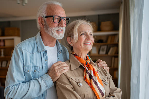 istock Happy senior couple looking out the window, embracing future together 2214077111