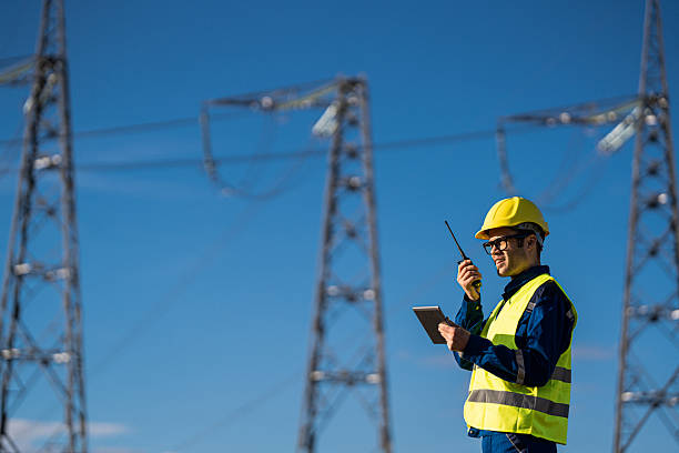 istock Technician communicates via radio in high-visibility vest near electrical pylons, under blue sky. 2214077465
