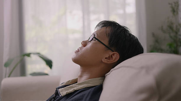 istock Asian Man Resting with Eyes Closed on Sofa in Quiet Living Space. 2214081392