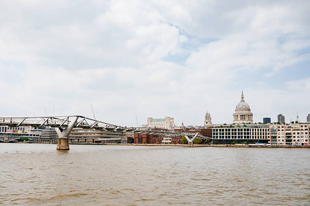 London, UK - July 19 2022: A woman shielding herself from the sun with an umbrella walks along Millennium Bridge during a heatwave in London. St Paul's Cathedral is seen in the background.