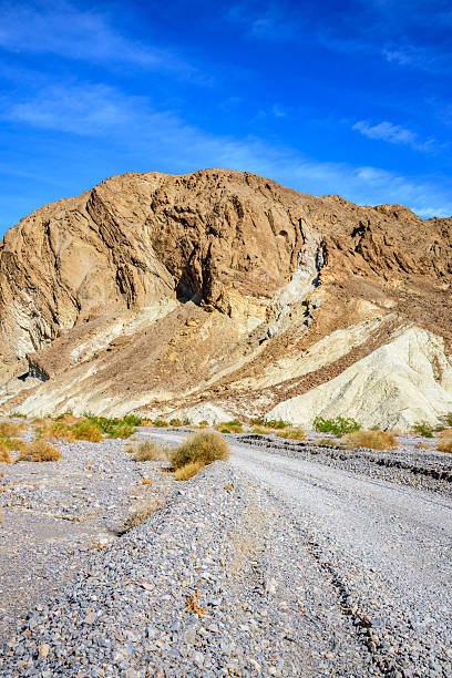 Looking across the entrance to Hole in the Wall Canyon, layers of golden sedimentary rock rise against the rugged peaks beyond. Shaped by ancient seas, earthquakes, and floods, this wild landscape reveals the raw geological history that makes Death Valley so extraordinary.  Hole in the Wall Canyon is in Death Valley National Park near Furnace Creek, California, USA.
