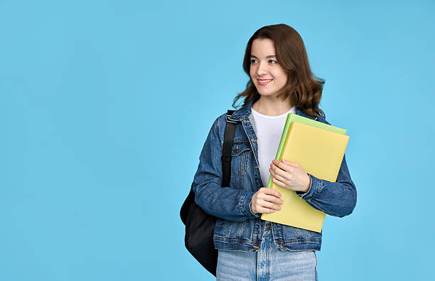 istock Pretty student girl holding notebooks and looking away, isolated on blue background. 2214101404