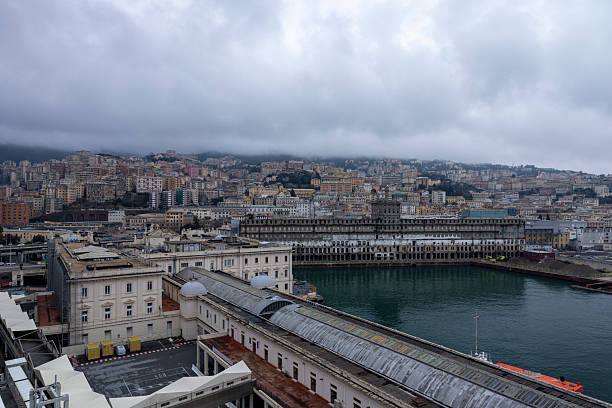 A panoramic view of Genova's harbor is showcasing historic buildings and urban landscape under a cloudy sky. The waterfront area is visible, featuring architectural details and serene water, creating a tranquil atmosphere.