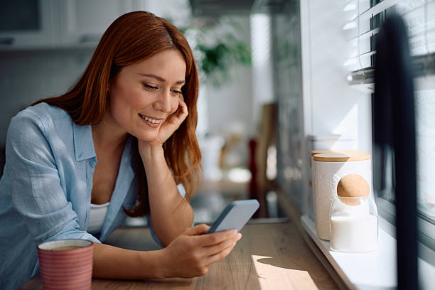 istock Happy woman reading message on cell phone in the kitchen. 2214112013