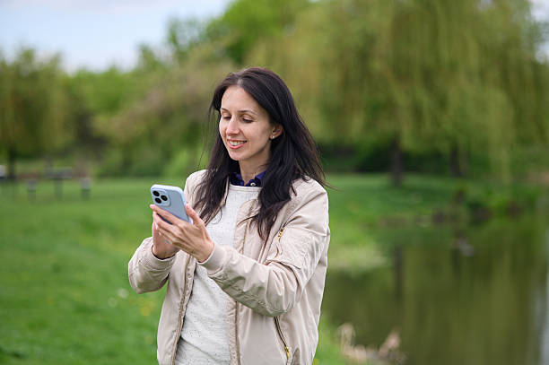 istock Smiling woman making a video call in park and pointing upward 2214120565