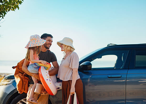 A cheerful family gathers near their car beside the sea, ready for a fun vacation. The sun shines brightly as they prepare with beach gear, symbolizing carefree summer days filled with joy.