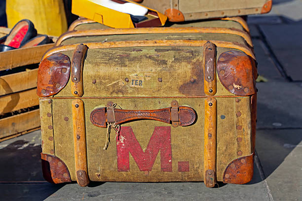 Old dark red leather suitcase with metal corners and a travel tag, placed inside a train compartment near wooden paneling and a heater.