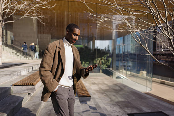 Stylish entrepreneur using smartphone outside modern office building