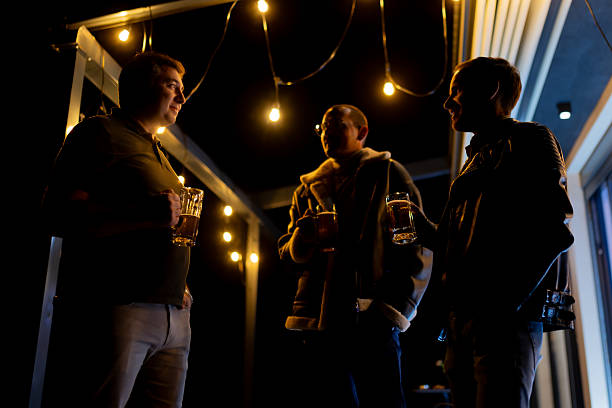 istock Three friends enjoying a night outdoors with beer and warm conversation under string lights 2214145712