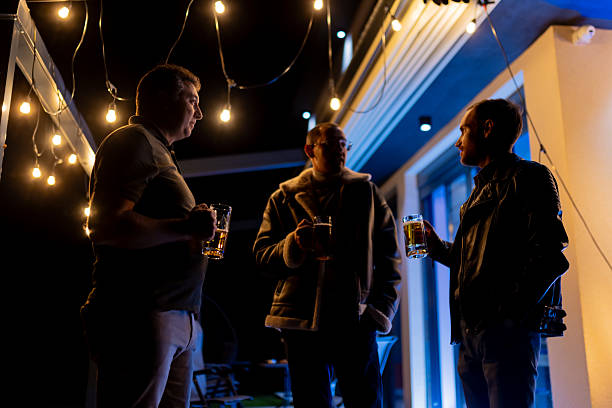 A group of friends enjoying drinks together outdoors at night illuminated by string lights, creating a warm and relaxed atmosphere. The scene conveys friendship, bonding, and cozy nightlife feelings.