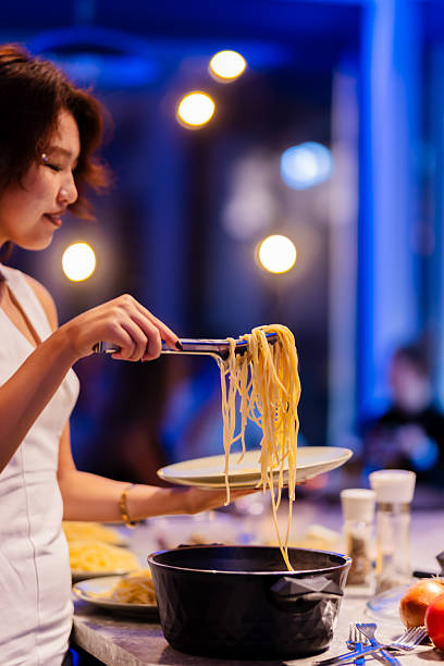 istock Woman serving spaghetti from a pot onto a plate in a bright kitchen environment 2214145747