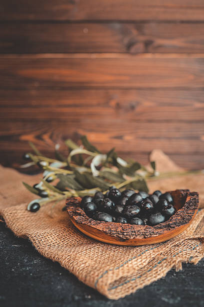 istock Rustic wooden bowl filled with glossy black olives on a burlap surface, with olive branches in the background. Warm natural light, traditional Mediterranean food concept 2214148147