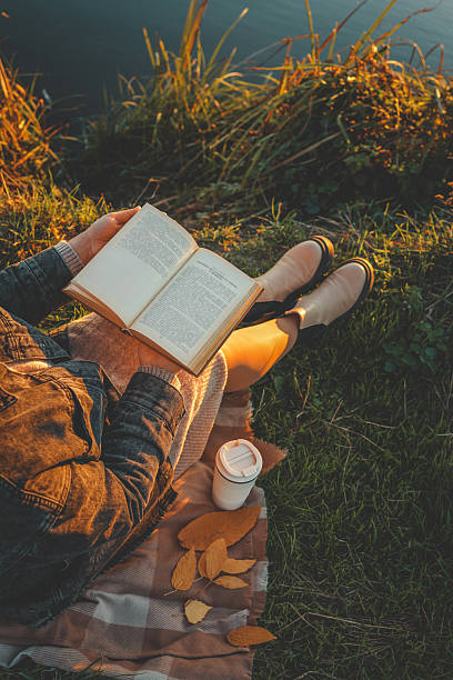 istock Girl by the river reading a book, beautiful sunset 2214148282