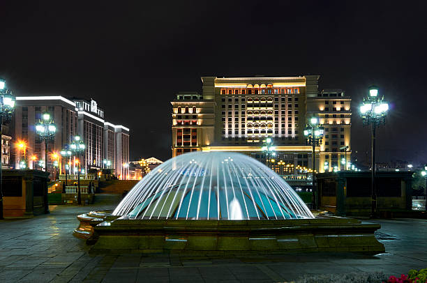 A large building with a fountain in front of it. The fountain is lit up at night. The building is a hotel