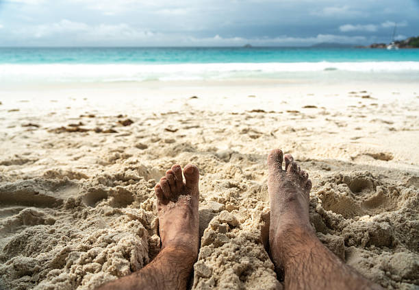 Person's feet are covered in sand while relaxing on a sunny beach, enjoying summer vacation. Film photo