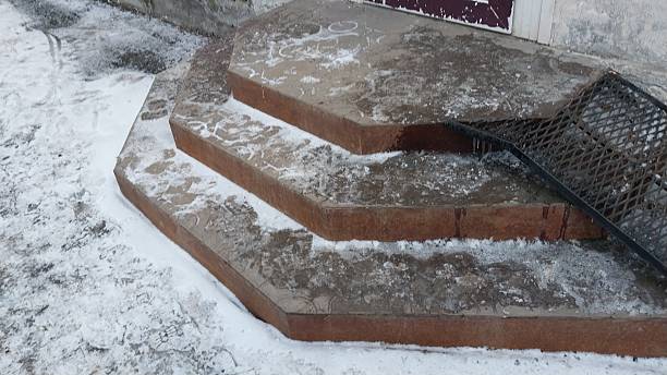 istock Three icy concrete steps with a black metal grate leaning against them, surrounded by a dusting of snow. 2214175130