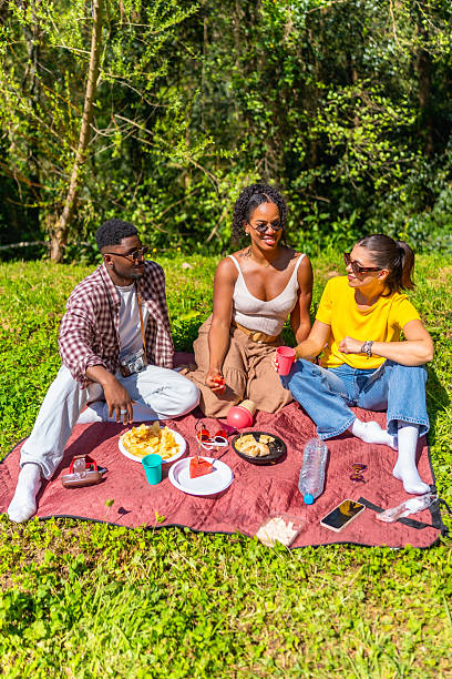 Group of friends enjoying a lively picnic in the park, sharing laughter while eating delicious food and sipping drinks under the sun