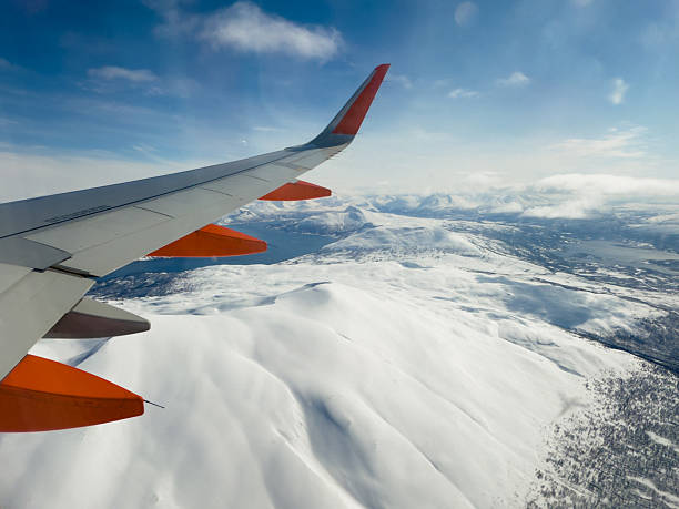 View from airplane window showing wing over snowy mountains. Scenic aerial shot capturing winter wilderness. Perfect for travel, adventure, and tourism themes.