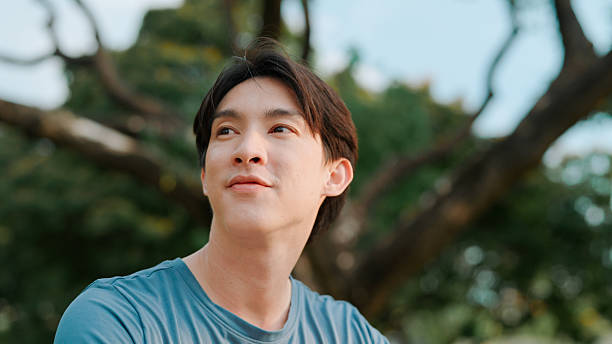 istock Asian man looking away in public park 2214182397
