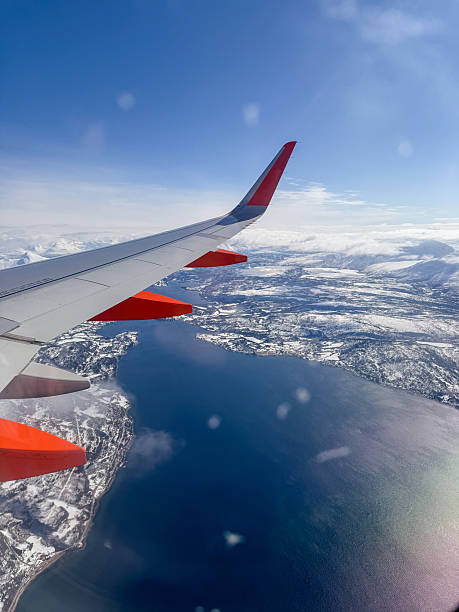 View from airplane window showing wing and snowy mountains. Stunning aerial landscape with clear blue sky. Perfect for travel enthusiasts and aviation-related content.