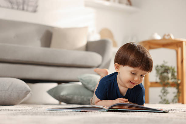 istock Cute little boy with book on floor at home, space for text 2214191154
