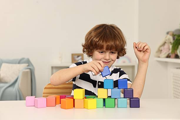 istock Little boy stacking colorful cubes at white table indoors 2214192095