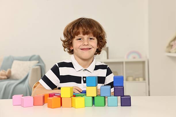 istock Little boy stacking colorful cubes at white table indoors 2214192099