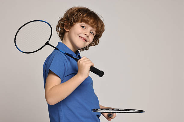 Little boy with badminton rackets on light grey background, space for text