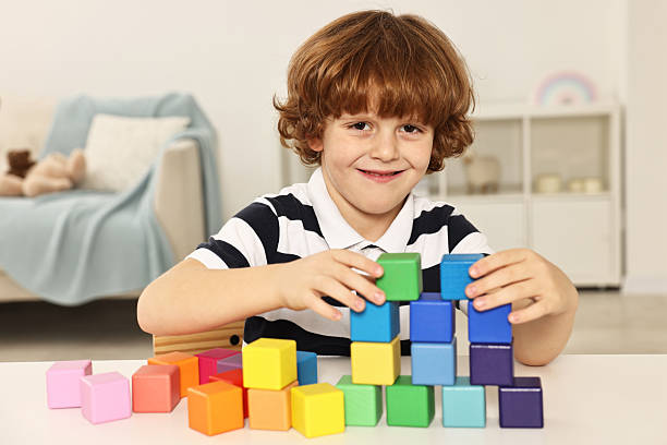 istock Little boy stacking colorful cubes at white table indoors 2214192288