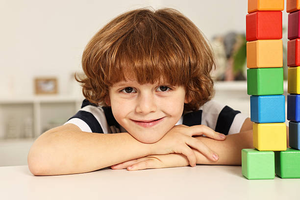 istock Little boy playing with stacked colorful cubes at white table indoors 2214192319
