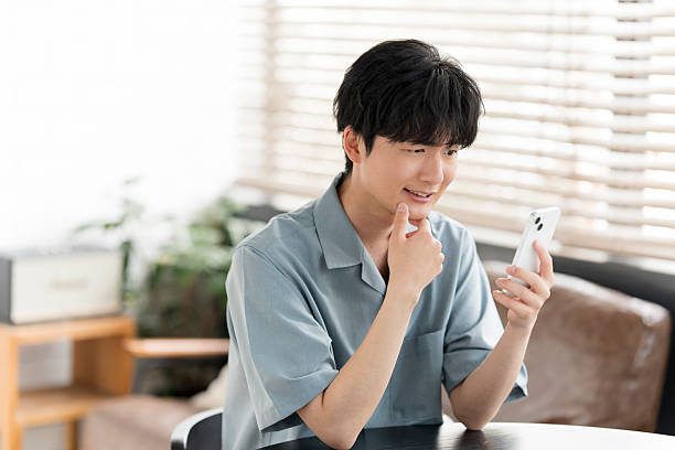 istock Young Japanese man looking at his smartphone at home 2214197726