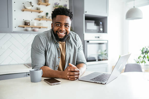 istock Smiling black businessman working on a laptop in a modern kitchen 2214201822