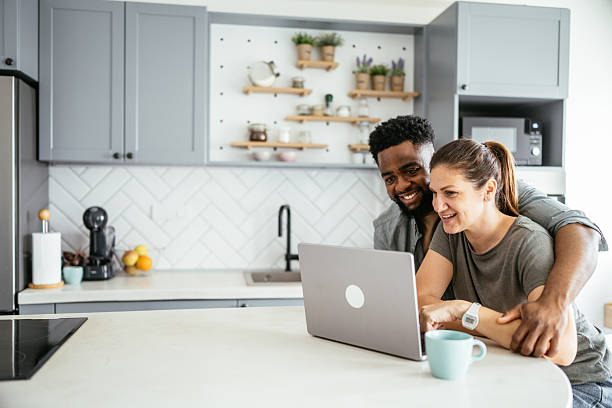istock Multiracial couple sits at a kitchen table working on a laptop, smiling and using internet 2214201835