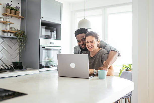 istock Multiracial couple sits at a kitchen table working on a laptop, smiling and using internet 2214201840