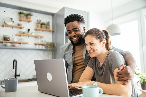 istock Multiracial couple sits at a kitchen table working on a laptop, smiling and using internet 2214201842