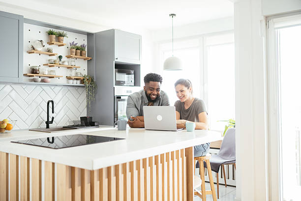 istock Multiracial couple sits at a kitchen table working on a laptop, smiling and using internet 2214201853