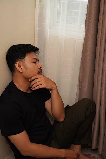 istock frustrated asian man holding head sitting on floor 2214202624