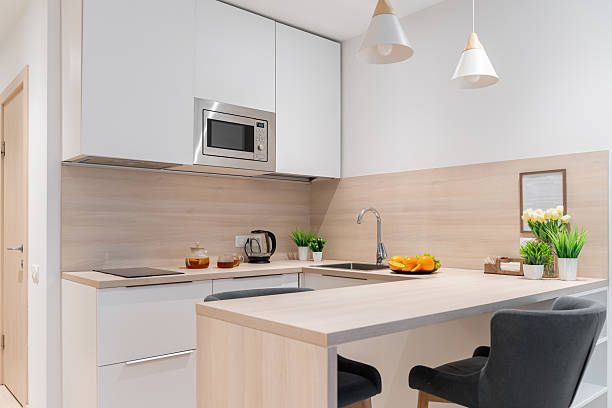 istock a small, bright kitchen with wooden countertops. built-in kitchen with lower and upper cabinets. There is a teapot and mugs of tea on the countertop, flowers in a vase, fruits on a plate. 2214204924